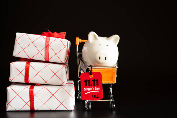 Online shopping of China, 11.11 single day sale concept. Red ticket 11.11 single day sale tag hanging with piggy bank on shopping cart with stack of gift boxes.