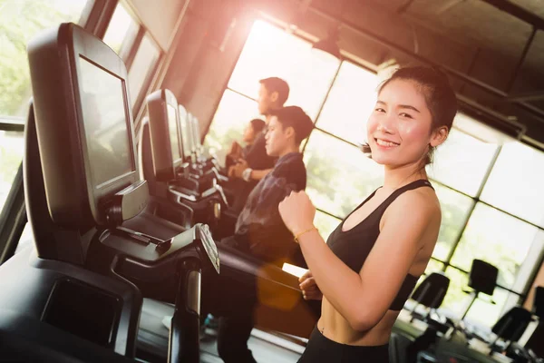 Happy asian woman with group of young people running or jogging on treadmills in modern sport gym. exercise and sport concept.