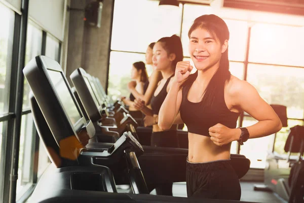 Happy woman with group of young people running or jogging on treadmills in modern sport gym. exercise and sport concept.