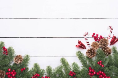 Noel ve yeni yıl kompozisyon. Beyaz ahşap masa arka plan üzerinde çam dalları, çam kozalakları, kırmızı meyveler ve çan üstten görünüm.