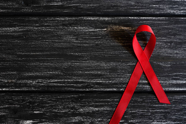 Closeup red ribbon awareness on black wooden table background  for World Aids day campaign.