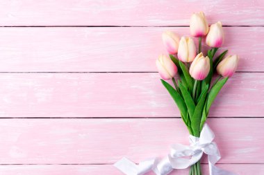 Sevgililer günü ve aşk kavramı. Pembe pastel ahşap arka plan üzerinde beyaz kurdele ile pembe laleler.
