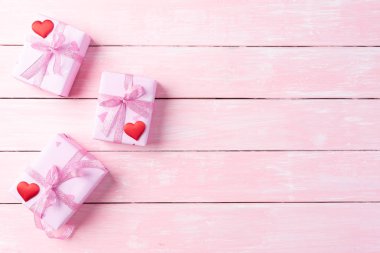 Valentines day and love concept. Pink gift box with red heart and flowers on pink wooden background.
