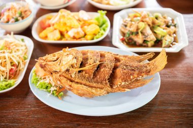 Fired fish with other delicious thai foods on wooden table.