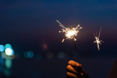 Mutlu sevimli kız bir maytap sahilde günbatımı sırasında holding. Kutlama kavramı.