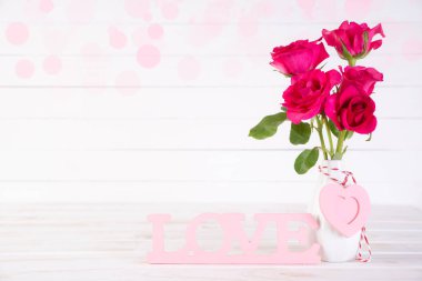 Sevgililer günü ve aşk kavramı. Pembe Gül Vazosu ahşap kalp ve ahşap harflerle kelime beyaz ahşap zemin üzerine yazılmış aşk şekillendirme.