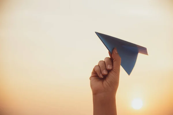 Woman Hand holding blue paper rocket with golden sky during sunset background. freedom concept.