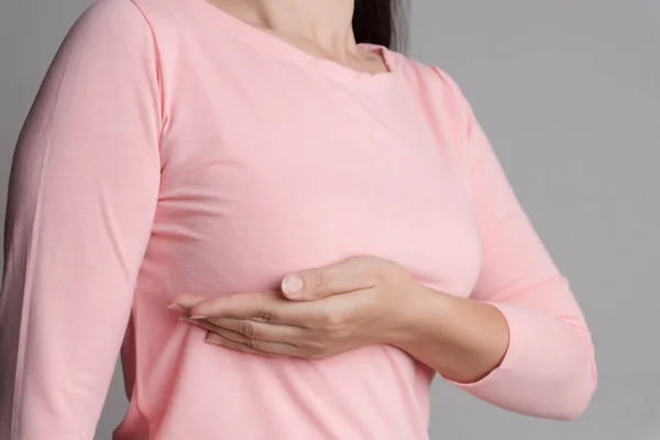 女性の手は 灰色の背景に乳がんの兆候のために彼女の胸の上に塊をチェックします 医療の概念 — ストック写真