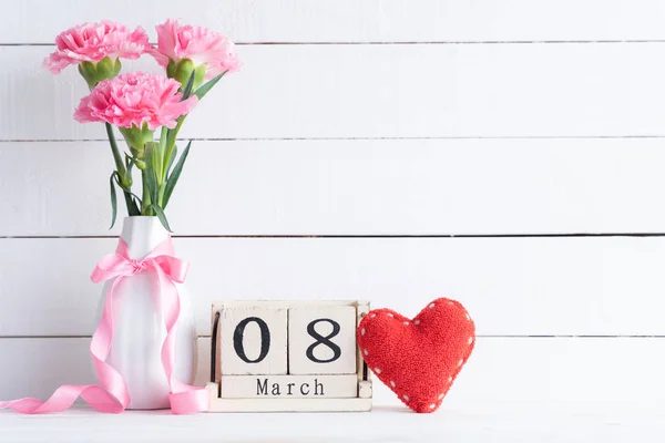女人的日子概念 粉红色康乃馨花在花瓶和红色心脏与3月8日文字在木块日历在白色木制背景 — 图库照片