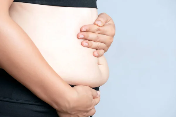 Tlustá ženská ruka drží nadměrné břišní tuk. Zdravotní péče a žena — Stock fotografie