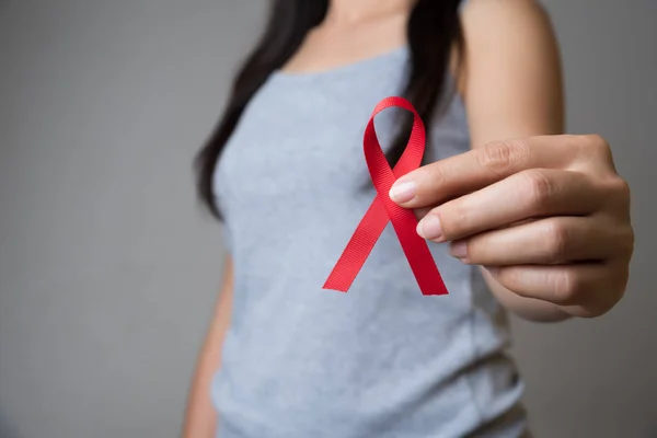 Closeup woman hand holding red ribbon HIV, world AIDS day awaren