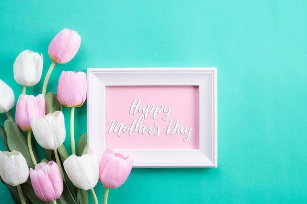 Happy mothers day concept. Top view of pink tulip flowers and white picture frame with happy mother's day text on green pastel background. Flat lay. — Stock Photo, Image