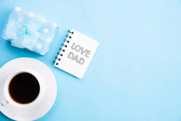 Concepto del día del padre feliz. Vista superior de la hermosa caja de regalo, taza de café con texto LOVE DAD sobre fondo pastel azul brillante . — Foto de Stock