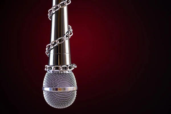 Microphone with a chain, depicting the idea of freedom of the press or freedom of expression on dark background. World press freedom day concept.