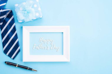 Mutlu babalar günü kavramı. Parlak mavi pastel arka plan üzerinde mutlu babalar günü metin ile mavi kravat, güzel hediye kutusu, kahve bardağı, beyaz resim çerçevesi üst görünümü.