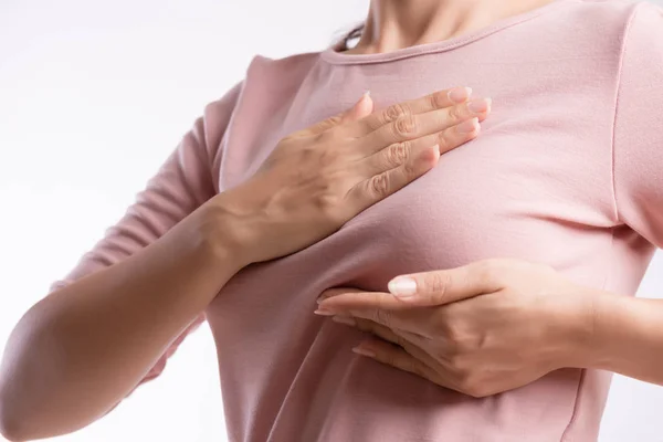 Mano de mujer revisando bultos en su pecho en busca de signos de cáncer de mama sobre fondo gris. Concepto sanitario. — Foto de Stock