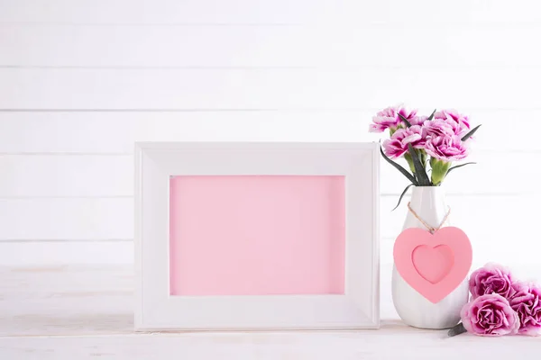 Marco de imagen blanco con hermosa flor de clavel rosa en jarrón sobre mesa de madera blanca . — Foto de Stock