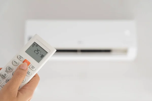 Mulher mão segurando controlador remoto dirigido sobre o ar condicionado dentro da sala e definido à temperatura ambiente, 25 graus celsius . — Fotografia de Stock