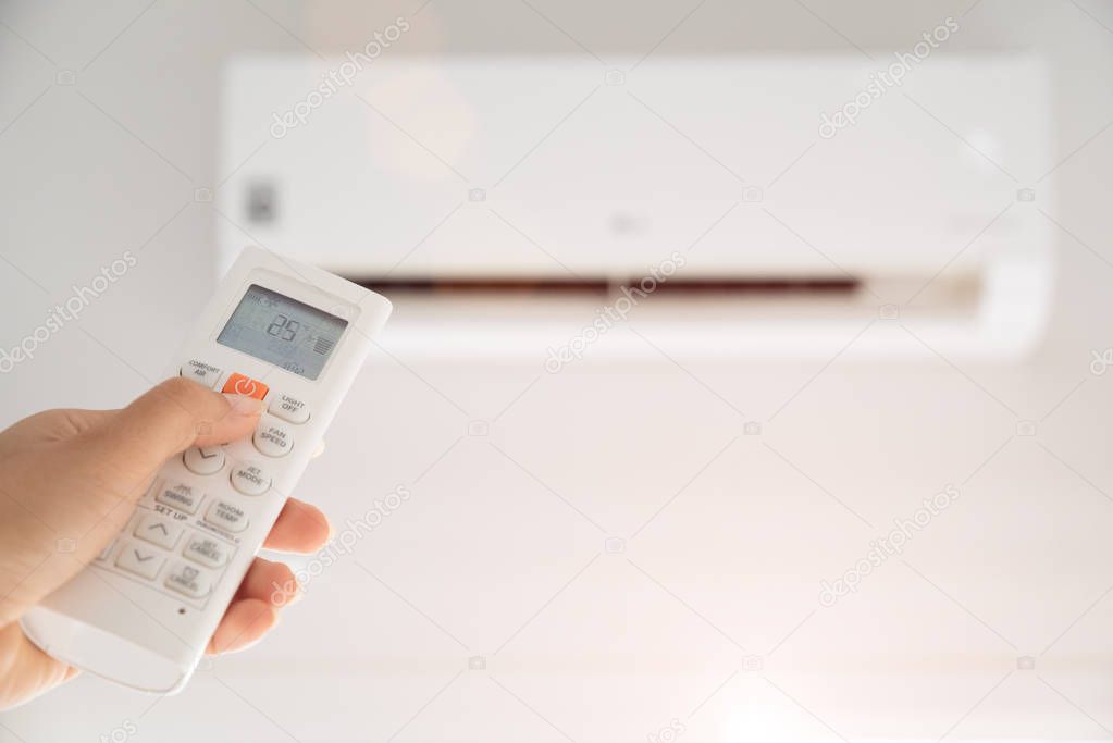 Woman hand holding remote controller directed on the air conditioner inside the room and set at ambient temperature,25 degrees celsius.