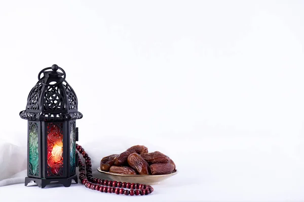 Ramadan food and drinks concept. Ramadan Lantern with arabian lamp, wood rosary, tea, dates fruit and lighting on a wooden table on white background.