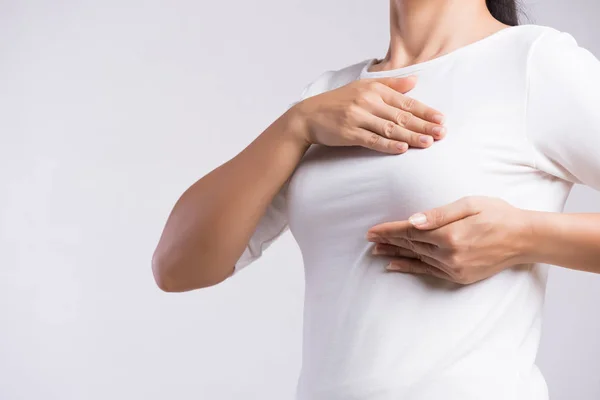 Mulher mão verificando pedaços em seu peito para sinais de câncer de mama em fundo cinza. Conceito de saúde. — Fotografia de Stock
