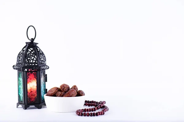 Ramadan food and drinks concept. Ramadan Lantern with arabian lamp, wood rosary, tea, dates fruit and lighting on a wooden table on white background.