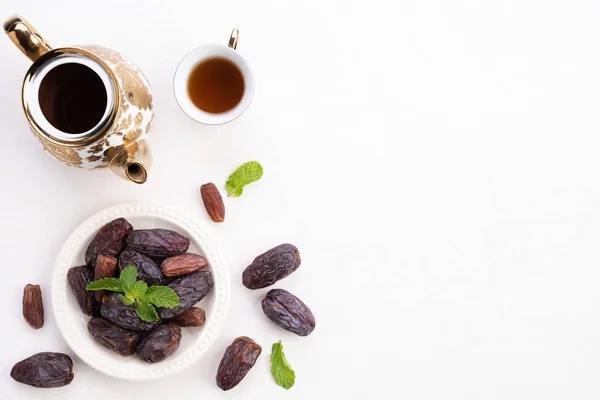 Ramadan food and drinks concept. Ramadan Lantern with tea, dates fruit, grape and Mint leaves on a white wooden table background. Top view, Flat lay.