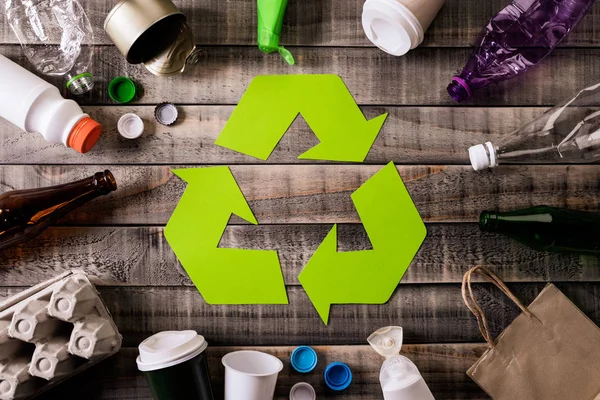 Widok z góry różnych materiałów odpadowych z symbolem recyklingu na tle tabeli. Recykling, środowisko i koncepcja eko — Zdjęcie stockowe