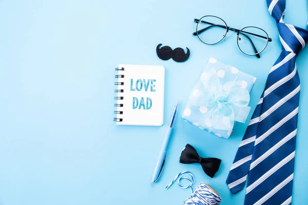 Concepto del día del padre feliz. Vista superior de corbata azul, hermosa caja de regalo, gafas con texto LOVE DAD sobre fondo pastel azul brillante. Puesta plana . — Foto de Stock