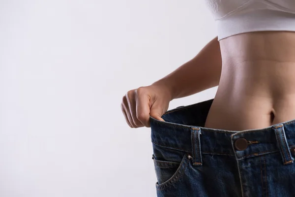 Ung smal kvinna i oversized blå jeans. Fit kvinna klädd för stora byxor. Healthcare och Woman diet livsstil koncept för att minska magen och forma upp friska magmuskler. — Stockfoto