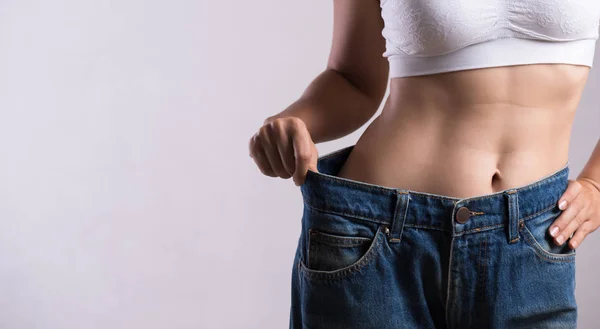 Mulher magra jovem em jeans azuis de grandes dimensões. Fit mulher vestindo calças muito grandes. Cuidados de saúde e conceito de estilo de vida da dieta da mulher para reduzir a barriga e moldar o músculo do estômago saudável . — Fotografia de Stock