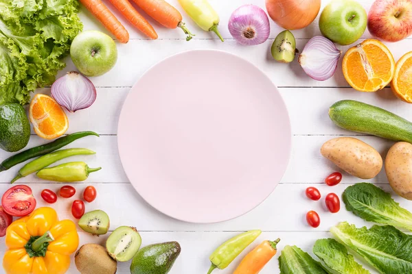 Estilo de vida saludable y concepto de comida. Vista superior de verduras frescas, frutas, hierbas y especias con un plato de pastel rosa vacío sobre fondo de madera blanca . — Foto de Stock