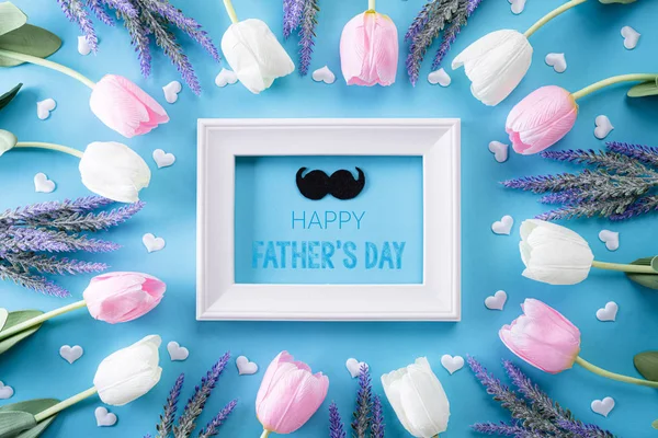 Happy fathers day concept. Top view of white pink tulip flowers and picture frame with Happy father\'s day text on bright blue pastel background. Flat lay.