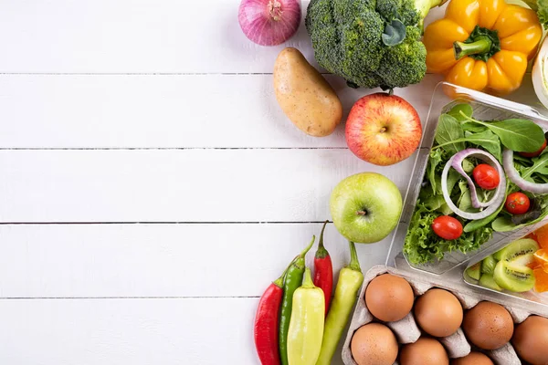 Un stil de viață sănătos și un concept alimentar. Vedere de sus a legumelor proaspete, fructelor, ierburilor și condimentelor cu o farfurie pastelată roz goală pe fundal din lemn alb . — Fotografie, imagine de stoc