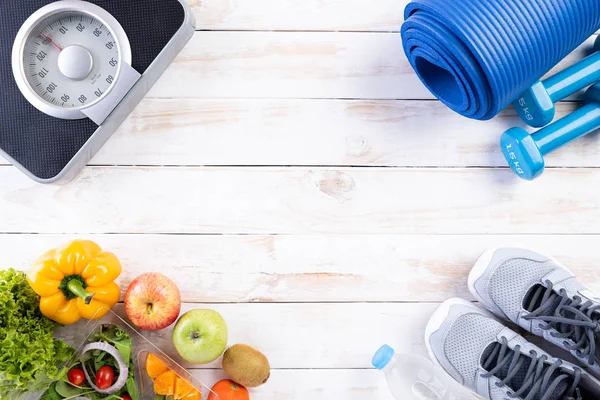Healthy lifestyle, food and sport concept. Top view of athlete's equipment Weight Scale measuring tape blue dumbbell, sport water bottles, fruit and vegetables on white wooden background.