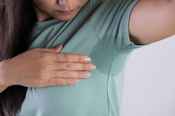 Close-up Aziatische vrouw met hyperhidrose zweten. Jonge Aziatische vrouw met zweet vlek op haar kleren tegen grijze achtergrond. Healthcare concept. — Stockfoto