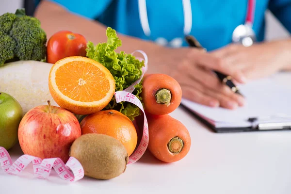 Healthy lifestyle, food and nutrition concept. Close up of fresh vegetables and fruits with stethoscope lying on doctor's desk. — Stock Photo, Image