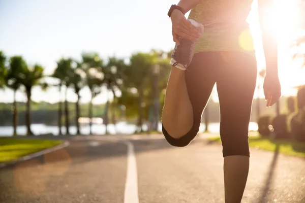 Joven corredor de fitness mujer estirando las piernas antes de correr en el parque. concepto de actividades de ejercicio al aire libre . — Foto de Stock