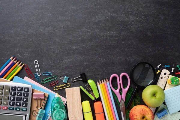 Eğitim ya da okula dönüş konsepti. Renkli okul malzemelerini kitaplar, renkli kalemler, hesap makinesi, ataçlar ve karatahta arka planında yeşil elma ile en üst düzeyde görmek. Düz yatıyordu. — Stok fotoğraf