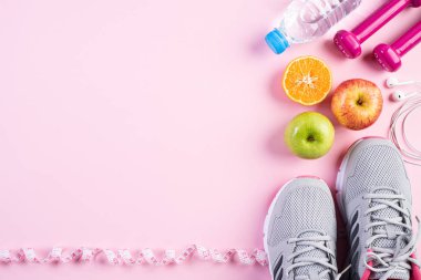 Sağlıklı yaşam tarzı, gıda ve spor konsepti. Pembe pastel arka plan üzerinde bant pembe dambıl, spor su şişeleri, spor ayakkabı ve yeşil elma ölçme atlet ekipman üst görünümü.