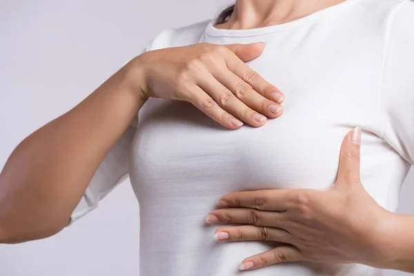 女性の手は、灰色の背景に乳がんの兆候のために彼女の胸の上に塊をチェックします.医療の概念. — ストック写真