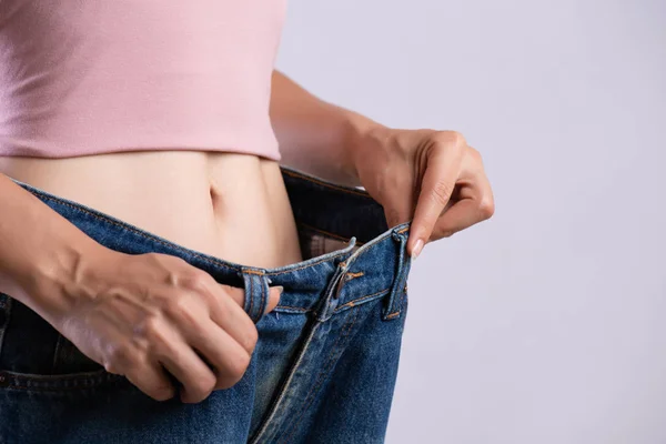 Ung smal kvinna i oversized blå jeans. Fit kvinna klädd för stora byxor. Healthcare och Woman diet livsstil koncept för att minska magen och forma upp friska magmuskler. — Stockfoto