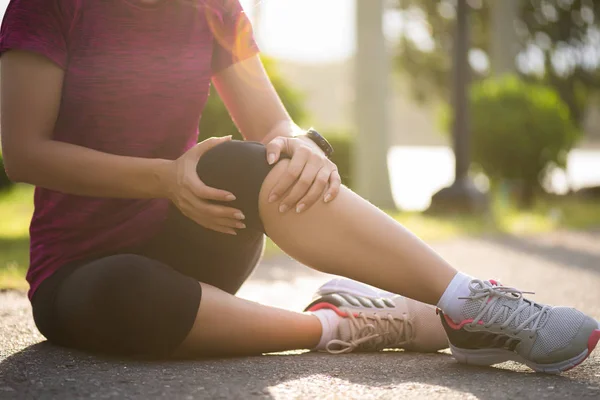 Young fitness woman runner feel pain on her knee in the park. Outdoor exercise activities concept.