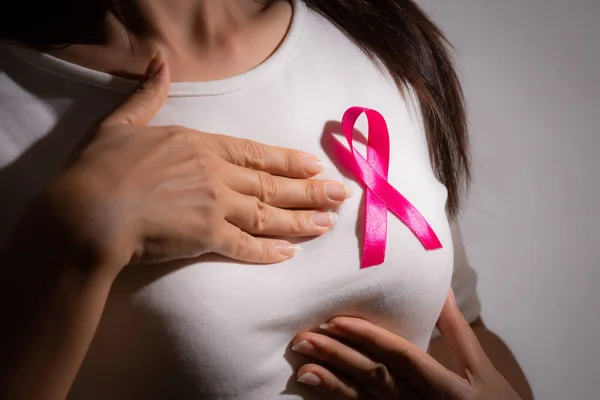 Closeup of pink badge ribbon on woman chest to support breast cancer cause. Healthcare, medicine and breast cancer awareness concept.