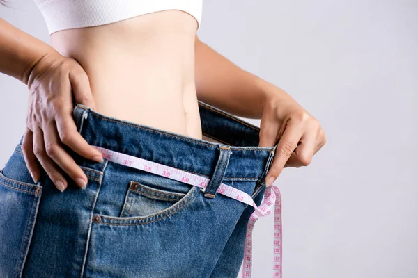 Feche a jovem magro medindo sua cintura fina com uma fita métrica. Cuidados de saúde e conceito de estilo de vida da dieta da mulher para reduzir a barriga e moldar o músculo do estômago saudável . — Fotografia de Stock