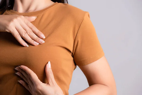 Frau überprüft Klumpen an ihrer Brust auf Anzeichen von Brustkrebs auf grauem Hintergrund. Gesundheitskonzept. — Stockfoto