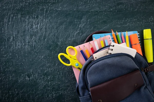 School backpack and school supplies with chalkboard background. Education or back to school concept.