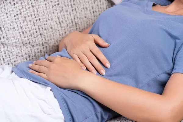 Jonge vrouw met pijnlijke buikpijn liggend op de Bank thuis. Chronische gastritis. Buik opgeblazen gevoel concept. — Stockfoto