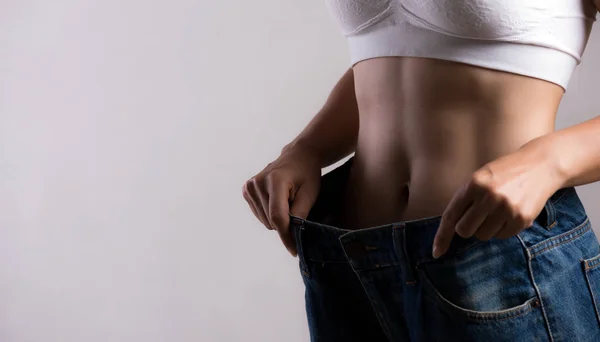 Ung smal kvinna i oversized blå jeans. Fit kvinna klädd för stora byxor. Healthcare och Woman diet livsstil koncept för att minska magen och forma upp friska magmuskler. — Stockfoto