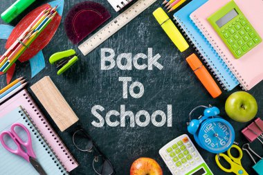 Eğitim ya da okula dönüş konsepti. Renkli okul malzemelerini kitaplar, renkli kalemler, hesap makinesi, ataçlar ve karatahta arka planında yeşil elma ile en üst düzeyde görmek. Düz yatıyordu.